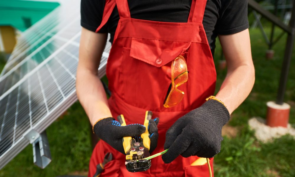 Close up of male hands in black gloves with equipment on blurry solar panels background.
